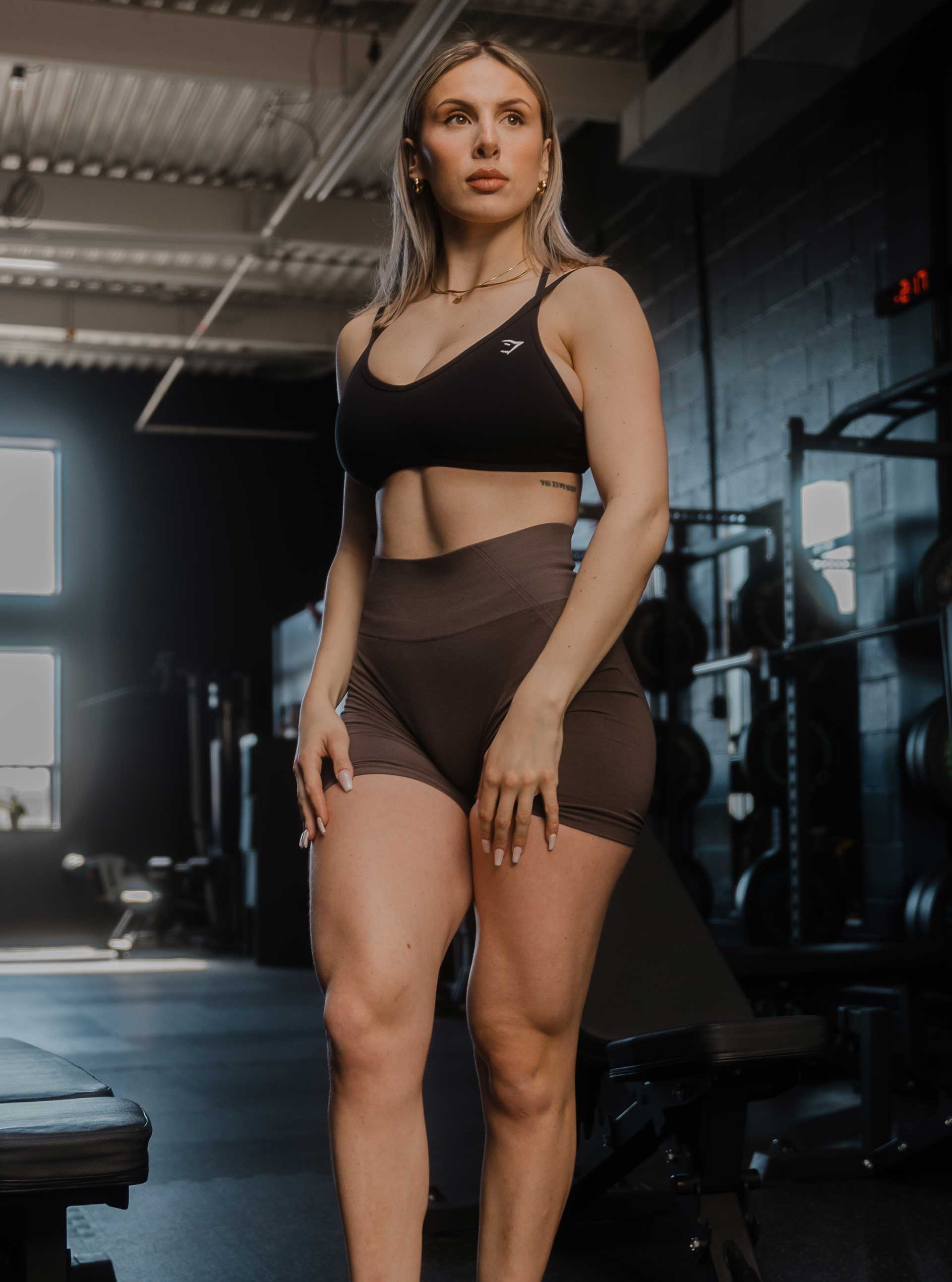 A coach posing confidently in a gym environment, surrounded by fitness equipment.